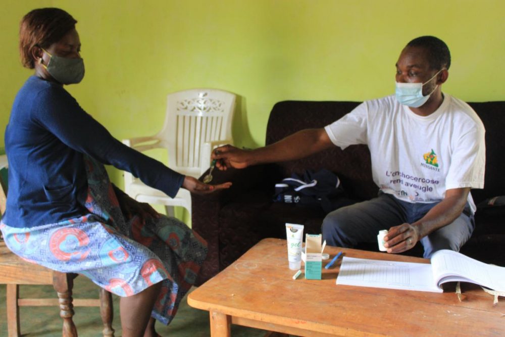 A man gives Mectizan pills to a woman in Cameroon. Both are wearing masks.