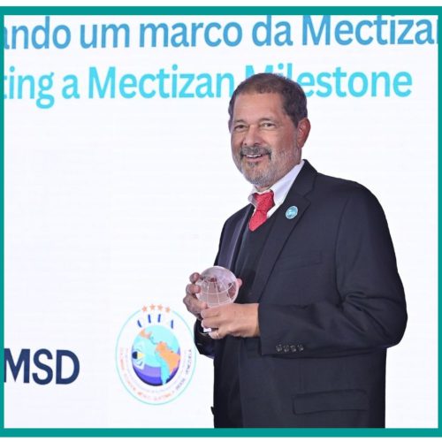 A man holds a glass trophy while standing in front of a banner reading Mectizan Milestone