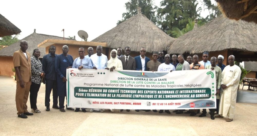 Group of people pose outdoors behind a banner reading in French: Fifth meeting of the technical committee of national and international experts on the elimination of lymphatic filariasis and onchocerciasis in Senegal